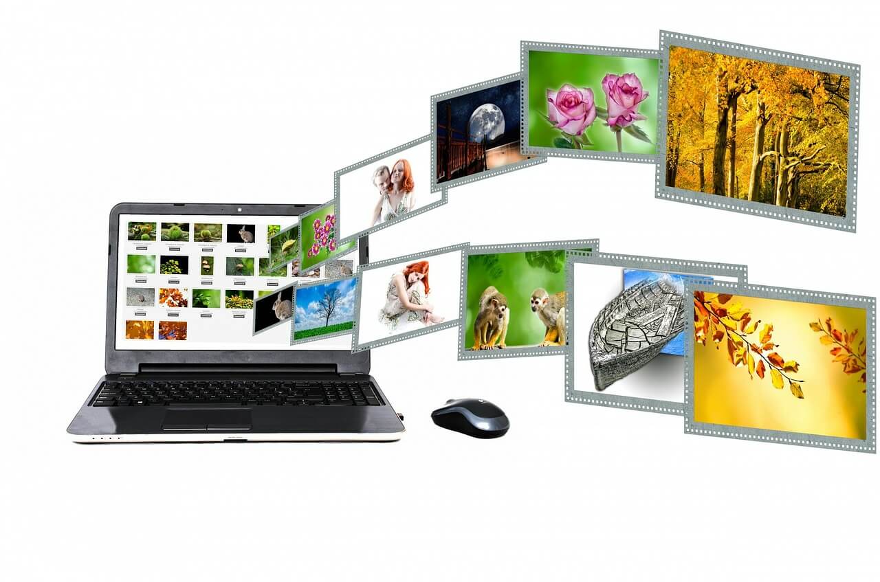 A mouse placed right next to a laptop. The screen of the laptop is full of images while many of them are flying out of the screen.